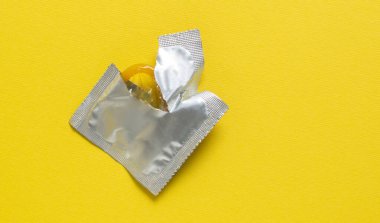 Sarı arka planda açık prezervatif ve prezervatif paketi. Hamilelik veya cinsel yolla bulaşan hastalık olasılığını azaltmak için kullanılan bir prezervatif. Güvenli seks ve üreme sağlığı kavramı.