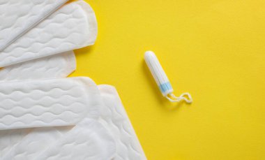 Sarı arka planda regl tamponları ve pedler. Adet döngüsü. Hijyen ve koruma.