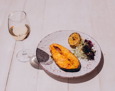 Glass of white wine and Fried salmon steaks with lemon on white plate