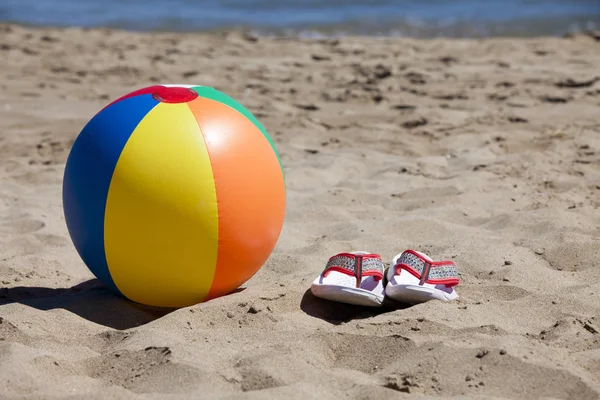 Strandbal en flip-flops in het zand — Stockfoto