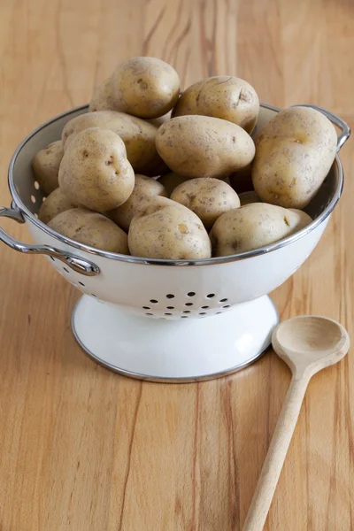 Weißer Emaille-Sieb mit rohen Kartoffeln und einem Kochlöffel — Stockfoto