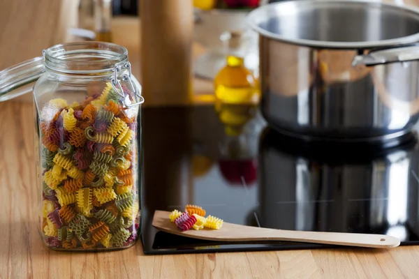 Barattolo di stoccaggio con pasta e cucchiaio da cucina sul piano di lavoro — Foto Stock