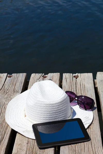 Tablet PC e chapéu de palha no lago de natação — Fotografia de Stock