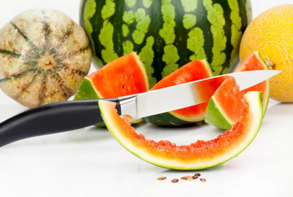 Verschillende meloenen en stukken met een keukenmes — Stockfoto