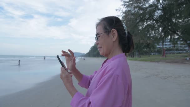 Tatil Konsepti Çözünürlük Sahilde Cep Telefonuyla Oynayan Yaşlı Bir Asyalı — Stok video