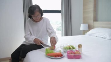 Sağlık konsepti 4k Çözünürlük. Yaşlı bir Asyalı kadın yatak odasında salata yapmaktan hoşlanır. sağlıklı yiyecekler.