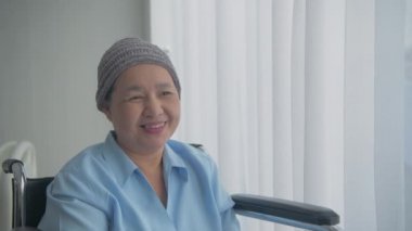 Sağlık konsepti 4k Çözünürlük. Hasta mutlu bir şekilde gülümsüyordu. Pencereden dışarı bak. Tekerlekli sandalyede oturan Asyalı kadın.