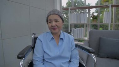 Sağlık konsepti 4k Çözünürlük. Hasta mutlu bir şekilde gülümsüyordu. Pencereden dışarı bak. Tekerlekli sandalyede oturan Asyalı kadın.