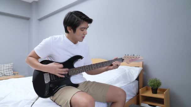 4K解像度の休日の概念 アジア人男性が寝室でエレキギターを練習している メロディーを学び — ストック動画