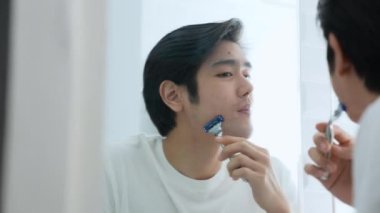 Sağlık konsepti 4k Çözünürlük. Genç Asyalı adam banyoda tıraş oluyor. Aynaya bak..