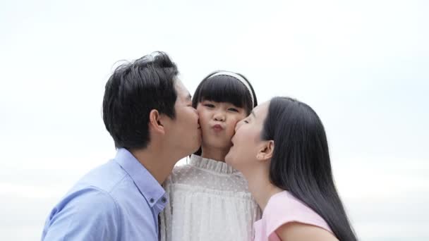 假日4K解像度的概念 父亲和母亲在海滩上亲吻女儿的脸颊 年轻的亚洲女孩笑得很开心 父母与子女关系 — 图库视频影像