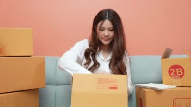 4k Kararlılığın iş konsepti. Asyalı kadın evdeki kutularda ürünleri paketliyor..