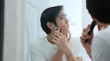 Sağlık konsepti 4k Çözünürlük. Genç Asyalı adam banyoda tıraş oluyor. Aynaya bak. elektrikli traş makinesi.