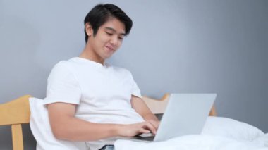 Tatil konsepti 4k Çözünürlük. Genç Asyalı adam yatak odasında çalışıyor..