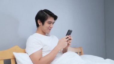 Tatil konsepti 4k Çözünürlük. Genç Asyalı adam yatak odasında cep telefonu çalıyor..