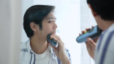 Sağlık konsepti 4k Çözünürlük. Genç Asyalı adam banyoda tıraş oluyor. Aynaya bak. elektrikli traş makinesi.