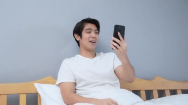 Tatil konsepti 4k Çözünürlük. Genç Asyalı adam yatak odasında cep telefonu çalıyor. iletişim teknolojisi.