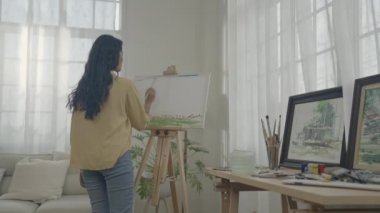 Sanatçı konsepti 4k Çözünürlük. Asyalı kadın oturma odasında resim çiziyor. Sanatçı iş yaratıyor. Boş zaman aktiviteleri ve hobileri.