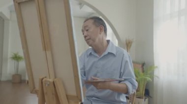 Sanatçı konsepti 4k Çözünürlük. Asyalı adam oturma odasında resim yapıyor. Sanatçı iş yaratıyor. Boş zaman aktiviteleri ve hobileri.