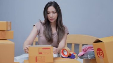 4k Kararlılığın iş konsepti. Asyalı kadın evdeki kutularda ürünleri paketliyor. Ürünlerin postaneden müşterilere dağıtımı.