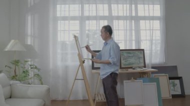 Sanatçı konsepti 4k Çözünürlük. Asyalı adam oturma odasında resim yapıyor. Sanatçı iş yaratıyor. Boş zaman aktiviteleri ve hobileri.