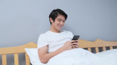 Tatil konsepti 4k Çözünürlük. Genç Asyalı adam yatak odasında cep telefonu çalıyor..