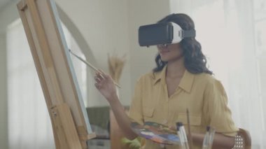 Sanatçı konsepti 4k Çözünürlük. VR giyip oturma odasında resim yapan Asyalı bir kadın. Sanatçı iş yaratıyor. Boş zaman aktiviteleri ve hobileri.
