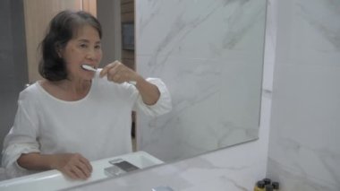 Sağlık konsepti 4k Çözünürlük. Asyalı yaşlı kadın banyoda dişlerini fırçalıyor..