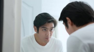 Sağlık konsepti 4k Çözünürlük. Asyalı adam banyoda yüzünü suyla yıkıyor. Derinin nemi ve tazeliği..