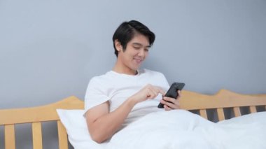 Tatil konsepti 4k Çözünürlük. Genç Asyalı adam yatak odasında cep telefonu çalıyor..