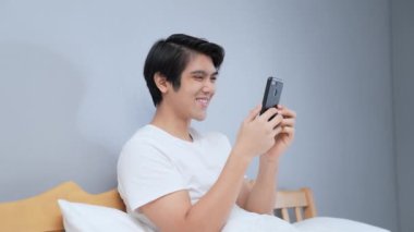 Tatil konsepti 4k Çözünürlük. Genç Asyalı adam yatak odasında cep telefonu çalıyor. iletişim teknolojisi.