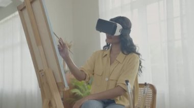 Sanatçı konsepti 4k Çözünürlük. VR giyip oturma odasında resim yapan Asyalı bir kadın. Sanatçı iş yaratıyor. Boş zaman aktiviteleri ve hobileri.