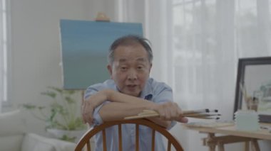 Sanatçı konsepti 4k Çözünürlük. Asyalı erkek sanatçı oturma odası sanatını nasıl yaratacağını anlatıyor. Boş zaman aktiviteleri ve hobileri.