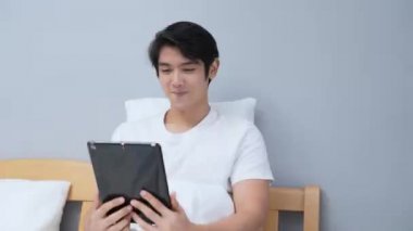 Tatil konsepti 4k Çözünürlük. Asyalı adam yatak odasında tablet oynuyor..