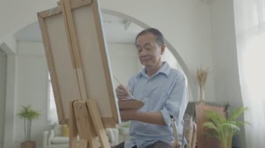 Sanatçı konsepti 4k Çözünürlük. Asyalı adam oturma odasında resim yapıyor. Sanatçı iş yaratıyor. Boş zaman aktiviteleri ve hobileri.