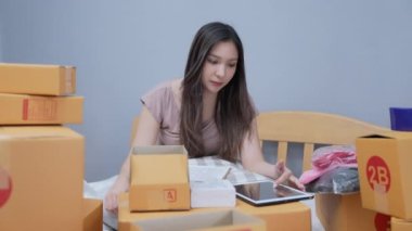 4k Kararlılığın iş konsepti. Asyalı kadın evdeki kutularda ürünleri paketliyor. Ürünlerin postaneden müşterilere dağıtımı.