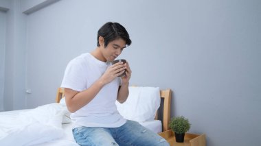 Tatil konsepti 4k Çözünürlük. Asyalı adam yatak odasında mutlu bir şekilde kahve içiyor. taze koku.