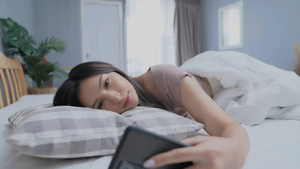 Holiday concept of 4k Resolution. Asian girls don\'t want to get out of bed in the morning. Mobile phone alarm. Laziness in waking up.