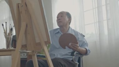 Sanatçı konsepti 4k Çözünürlük. Asyalı adam oturma odasında resim yapıyor. Sanatçı iş yaratıyor. Boş zaman aktiviteleri ve hobileri.