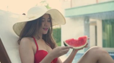 Holiday concept of 4k Resolution. Asian woman in bikini eating watermelon by the pool.
