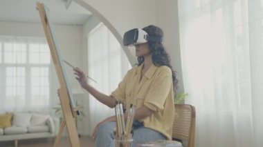 Sanatçı konsepti 4k Çözünürlük. VR giyip oturma odasında resim yapan Asyalı bir kadın. Sanatçı iş yaratıyor. Boş zaman aktiviteleri ve hobileri.