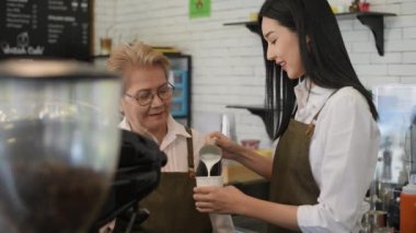 Coffee shop concept of 4k Resolution. An old woman teaching a young female employee to make coffee in a shop.