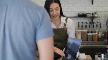 Coffee shop concept of 4k Resolution. Asian female staff are introducing menus to customers and paying by tablet.