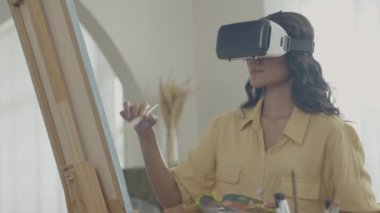 Sanatçı konsepti 4k Çözünürlük. VR giyip oturma odasında resim yapan Asyalı bir kadın. Sanatçı iş yaratıyor. Boş zaman aktiviteleri ve hobileri.