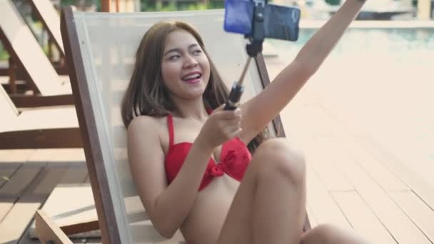 4K解像度の休日の概念 ビキニのアジア人女性はプールによって携帯電話でライブビデオ通話を持っています — ストック動画