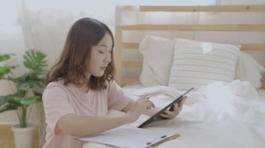 Holiday concept of 4k Resolution. Asian woman playing tablet in bedroom.