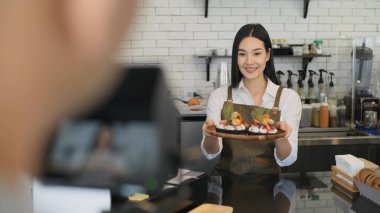 Kafe konsepti 4k Kararlılık. Asyalı kadın çalışan sosyal medyada pasta eleştirisi yapıyor.