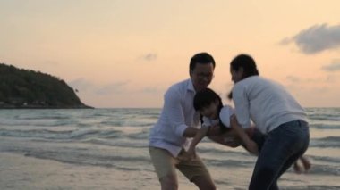 Tatil konsepti 4k Çözünürlük. Ebeveynler sahilde kızlarıyla oynuyorlar. Asyalı kız uçmak için elini hareket ettiriyor.