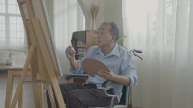 Sanatçı konsepti 4k Çözünürlük. Asyalı adam oturma odasında resim yapıyor. Sanatçı iş yaratıyor. Boş zaman aktiviteleri ve hobileri.
