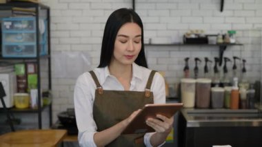 Coffee shop concept of 4k Resolution. Asian woman checking merchandise in a store using a tablet.